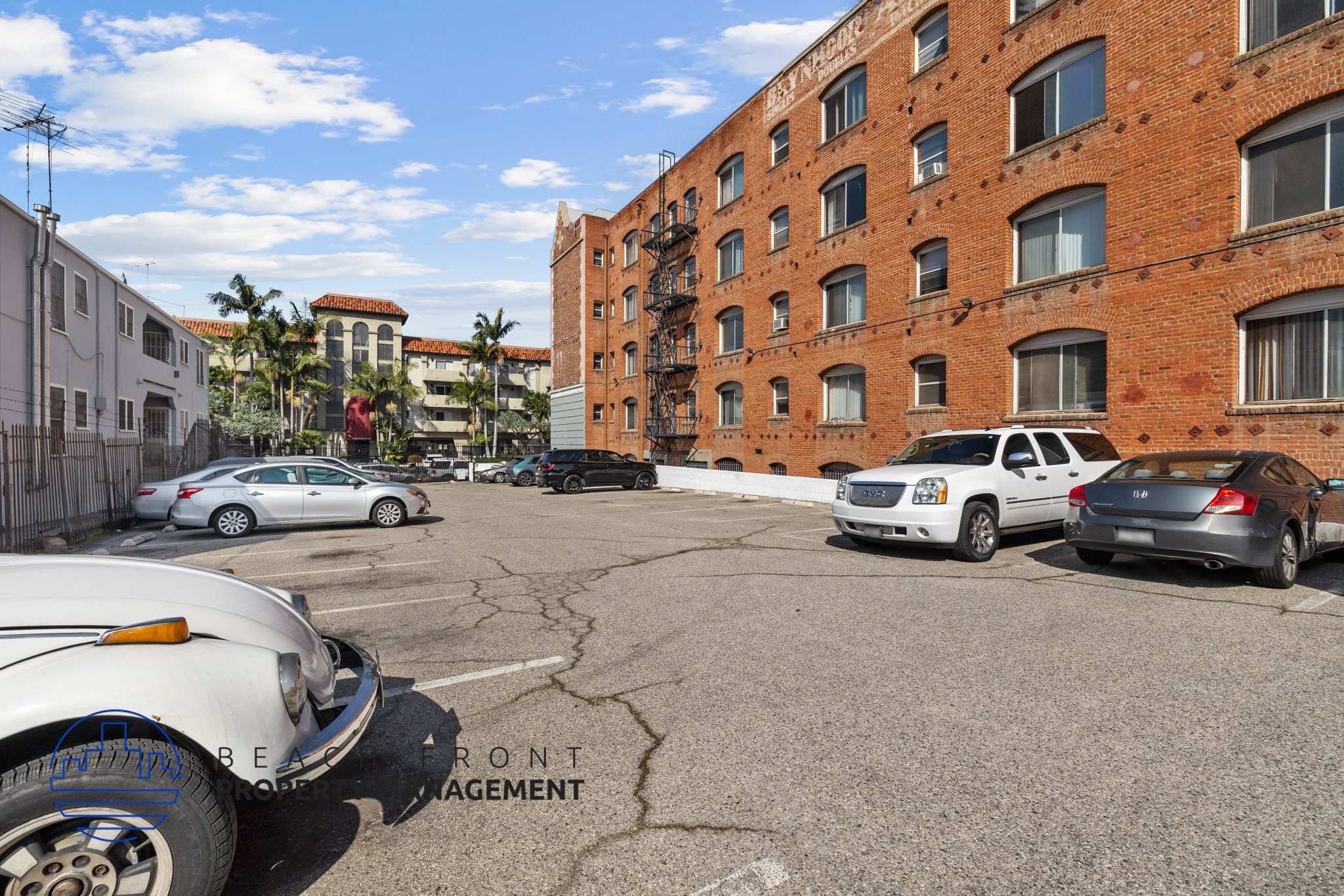 A parking lot with a white car in front and a red brick building in the background.